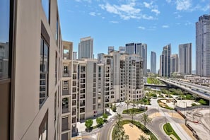 Un immeuble résidentiel de grande hauteur, doté de nombreux balcons, d’une cour aménagée et offrant une vue sur un paysage urbain avec des gratte-ciel modernes.
