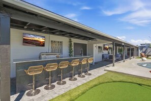 A modern outdoor bar area with a pool, bar stools, and a view of the sunset. - Spectacular Retreat with Private Pickleball Court (Tucson)