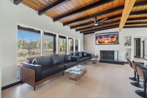 A modern living room with a black leather sofa, a glass coffee table, and a fireplace. - Spectacular Retreat with Private Pickleball Court (Tucson)