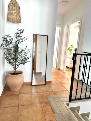 A hallway with a large potted plant, a mirror, and a staircase with a black railing. - Apartment 'Burriana Bliss Nerja' with Mountain View, Wi-Fi and Air Conditioning (Nerja)