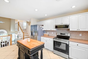 A modern kitchen with white cabinets, a stainless steel refrigerator, a microwave, an oven, and a wooden table with a jar on it. - Moore Fun by Brunswick Vacation Rentals - Canal Front Oasis w/ Pool & Tiki Bar (Ocean Isle Beach)
