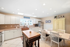 A kitchen with white cabinets, a wooden table, and a sign that reads 'Welcome to our Beach House.' - Moore Fun by Brunswick Vacation Rentals - Canal Front Oasis w/ Pool & Tiki Bar (Ocean Isle Beach)