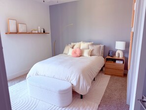 A bedroom with a bed, bedside table, lamp, and a shelf with decorative items. - Midtown Atlanta Luxury 1BR Skyline Views, Pool & Gym (Atlanta)