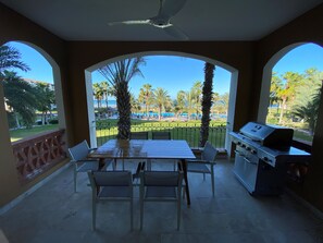 Um pátio ao ar livre com mesa e cadeiras, churrasqueira e vista para a praia e palmeiras.