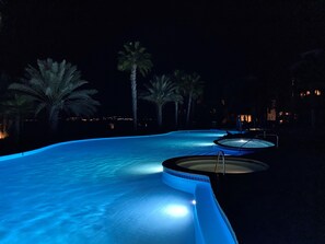 Piscina noturna com design curvo, cercada por palmeiras e um céu escuro.