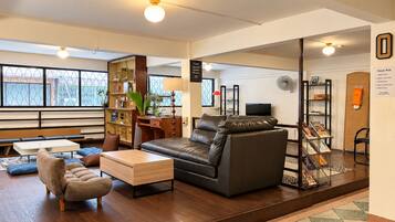 A modern living room with a sofa, armchair, and coffee table. There is a bookshelf, a desk, and a television.