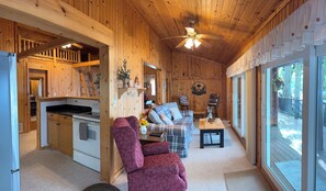 A cozy cabin interior with a kitchen, a plaid sofa, and a wooden ceiling.