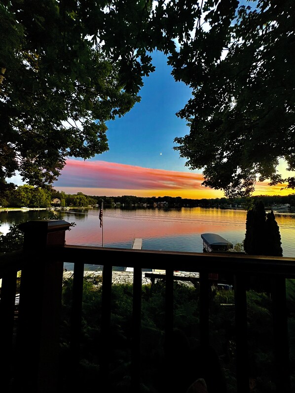 Vista de un lago con un muelle, árboles y cielo despejado.
