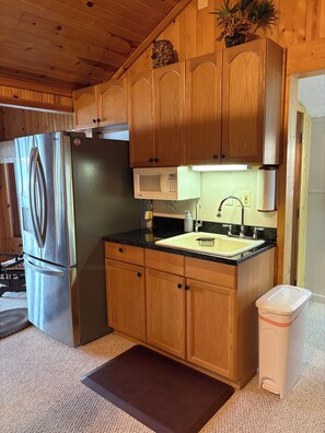 Una cocina compacta con armarios de madera, un refrigerador de acero inoxidable, un microondas y un lavamanos.