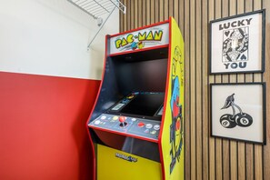 Ein Pac-Man-Spielautomat mit Bedienfeld, vor einer Wand mit Holzvertäfelung und gerahmten Kunstwerken.