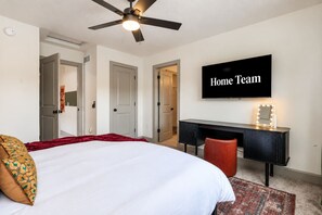 Ein Hotelzimmer mit einem Bett, einem Schreibtisch mit Spiegel und einem an der Wand befestigten Fernseher.