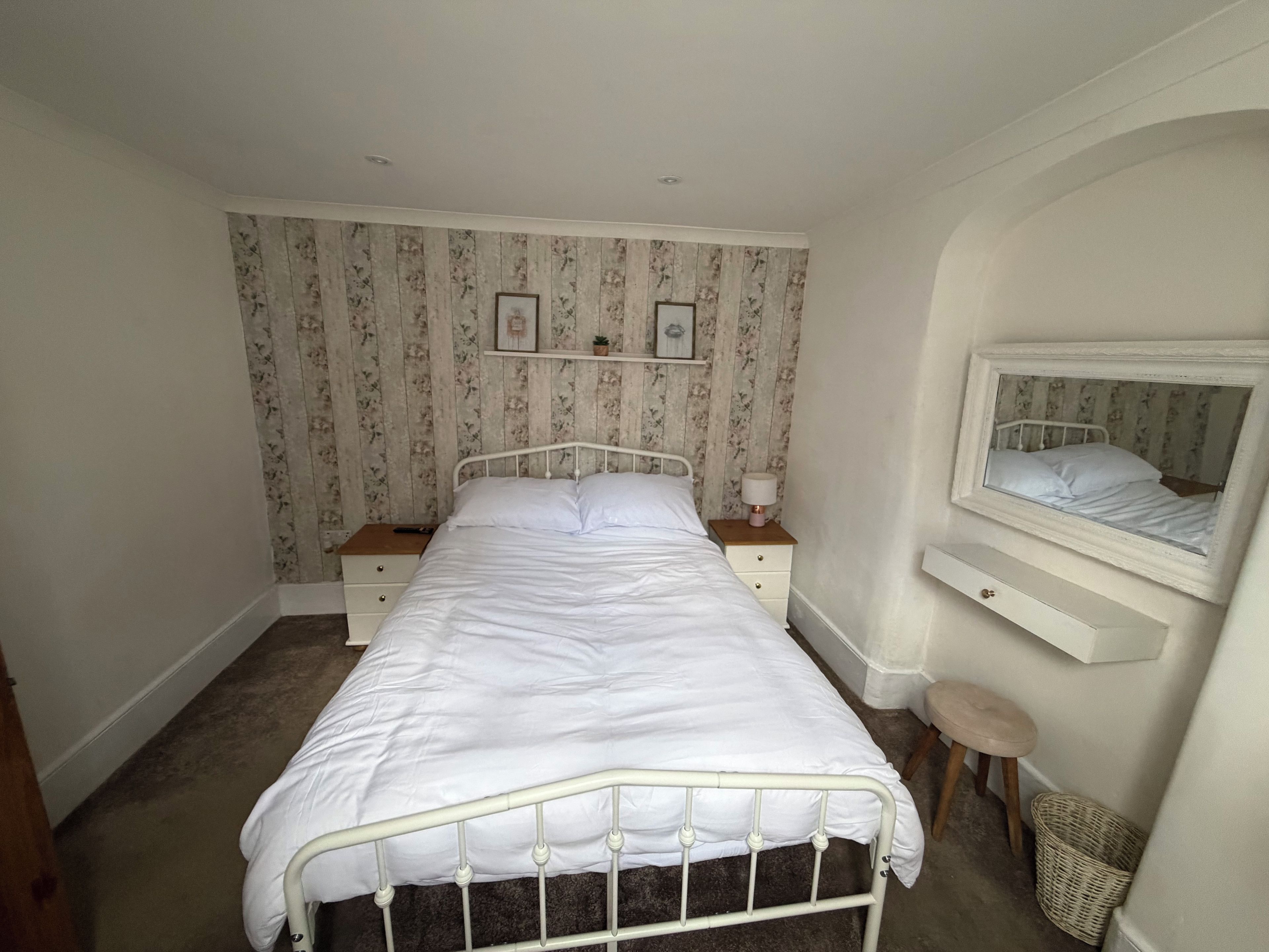 A bedroom with a single bed, bedside tables, a mirror, and a small stool.