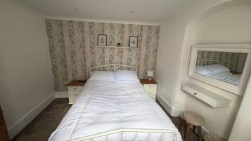 A bedroom with a single bed, bedside tables, a mirror, and a small stool.