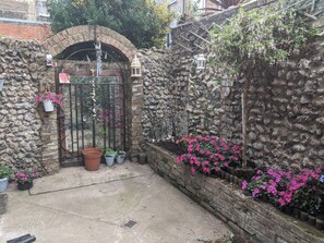 Un muro de piedra con una verja de metal, plantas en macetas y faroles colgantes.