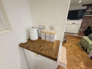 A kitchen area with a wooden countertop, a kettle, and labeled storage boxes for tea, coffee, and sugar. - Muckoroos Cottage | Historic Flint Cottage (Ramsgate)