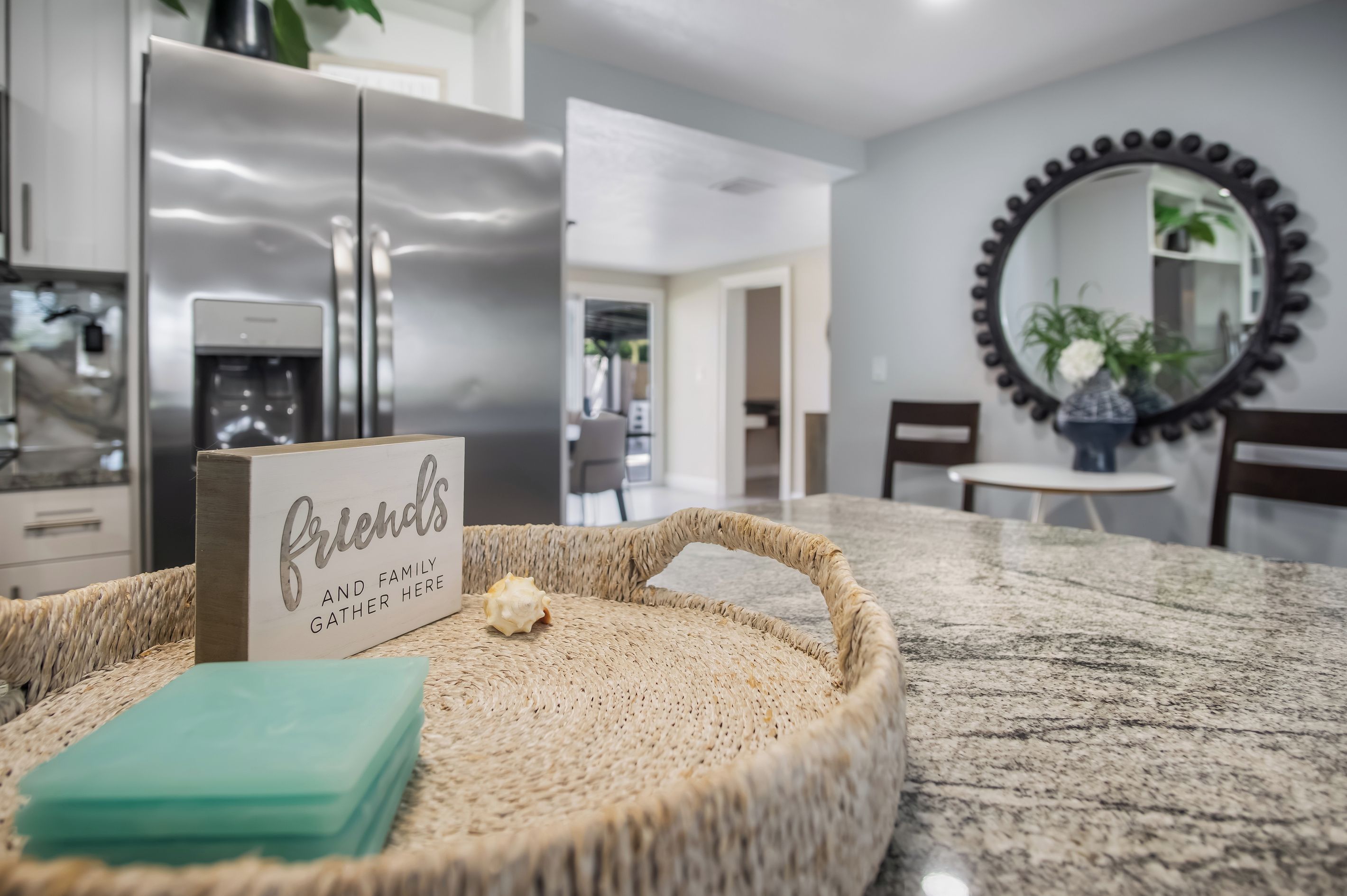 A kitchen area with a stainless steel refrigerator, a wicker tray with a card, and a marble countertop.