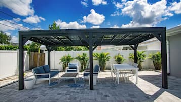 Ein überdachter Patio-Bereich mit Gartenmöbeln, einem Tisch und einer Pergola.