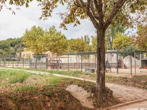 A fenced outdoor area with a dirt path, trees, and a building in the background. - Apartment 'Mas Moré Petit' with Shared Pool, Wi-Fi and Air Conditioning (Vulpellac)
