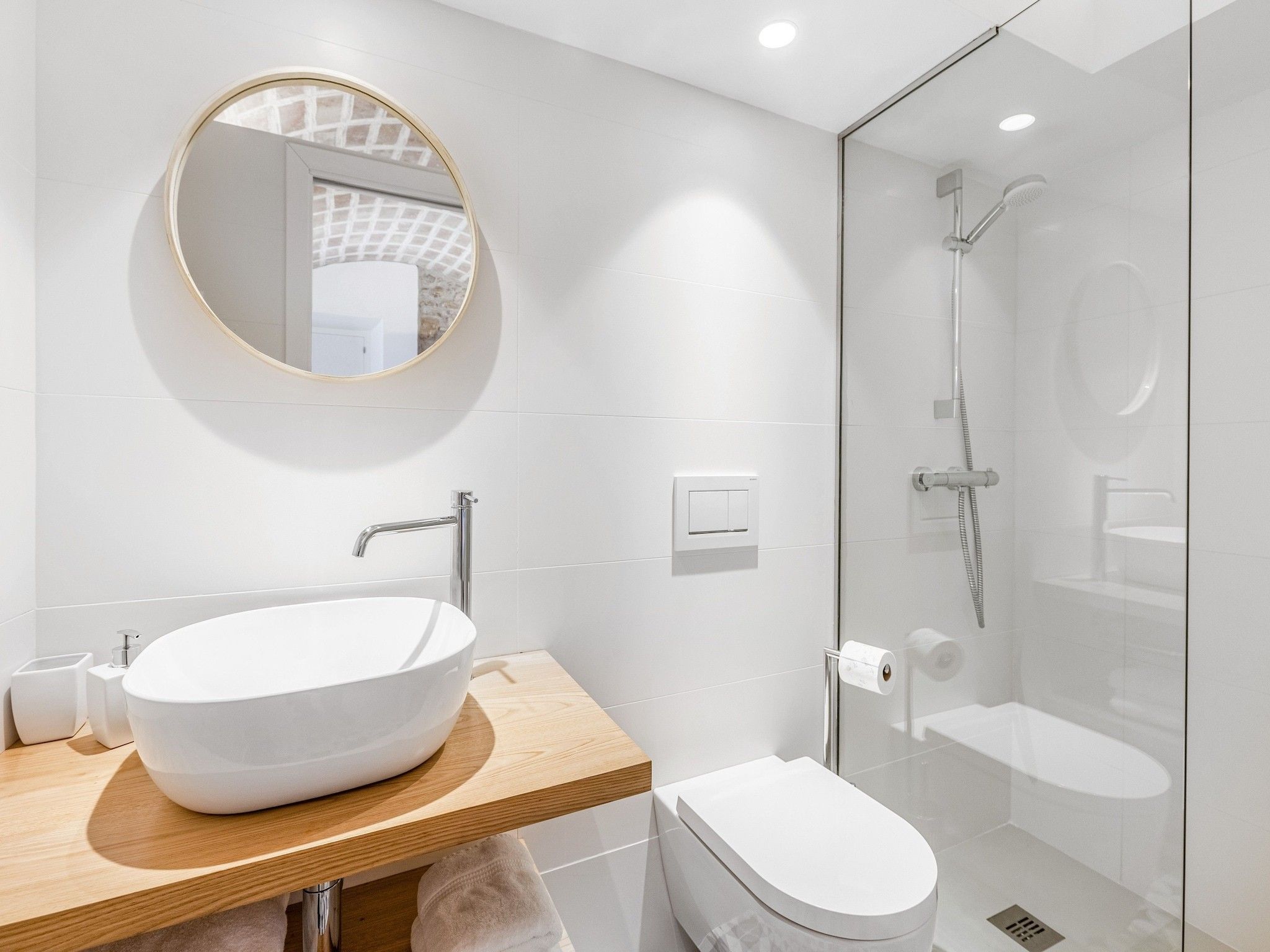 Une salle de bain moderne avec un grand lavabo ovale, un miroir rond, des toilettes et une douche séparée par une paroi de verre.