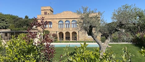 A large building with multiple arches and a tower, surrounded by well-maintained greenery and a pool.