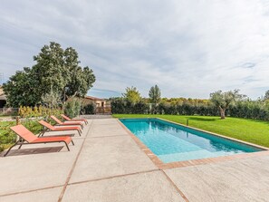 Une piscine avec des chaises longues, une terrasse dallée et une pelouse bien entretenue.