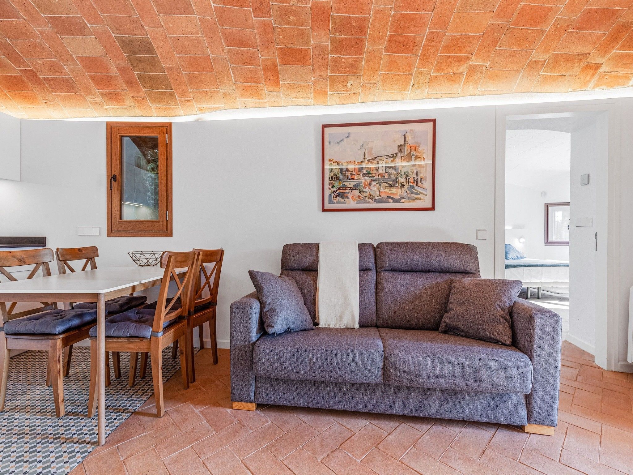 Una sala de estar con sofá, una mesa de comedor y sillas, y un cuadro en la pared.