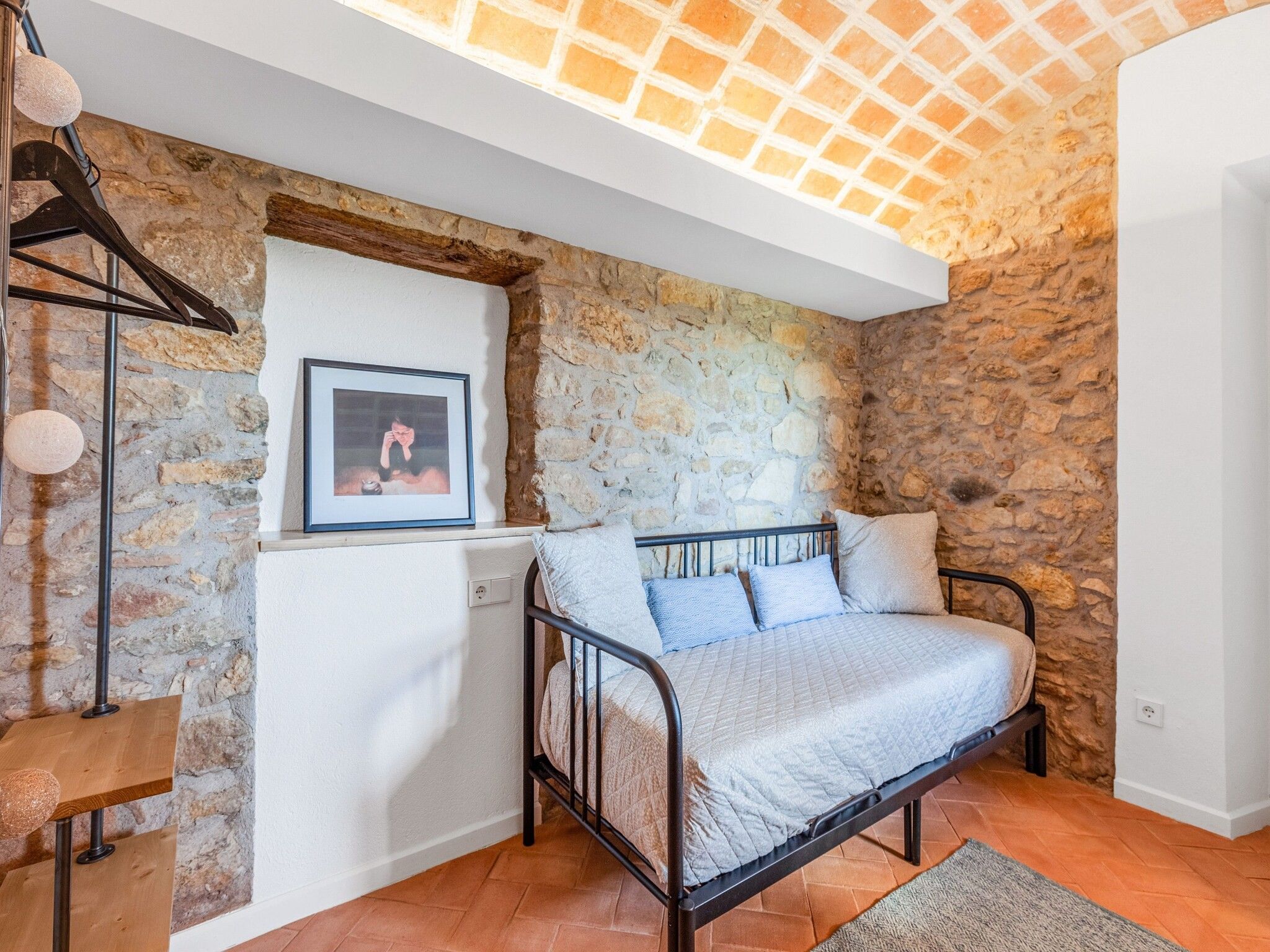 A bedroom with a stone wall, a bed with pillows, a framed picture on the wall, and a wooden floor.