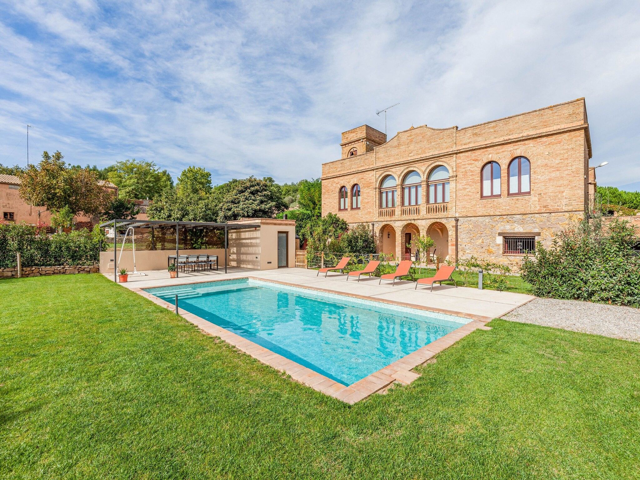 Una piscina con zona ajardinada, un porche cubierto y un edificio con ventanas de arco y una torre.