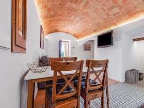 A dining area with a brick ceiling, a table, two wooden chairs, a television, and a patterned floor. - Apartment 'Mas Moré Petit' with Shared Pool, Wi-Fi and Air Conditioning (Vulpellac)