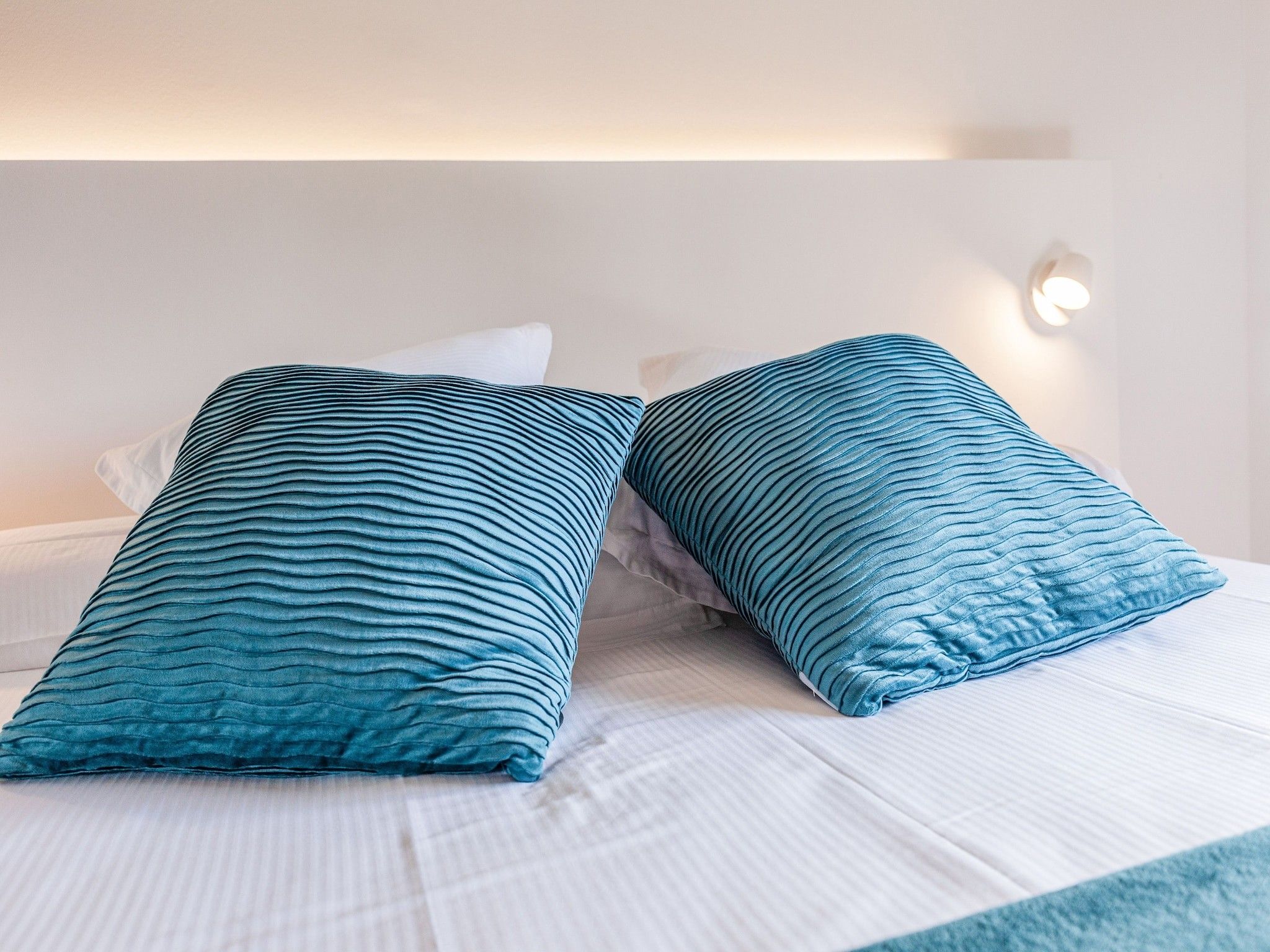 Een bed met twee kussens en een wandlamp.