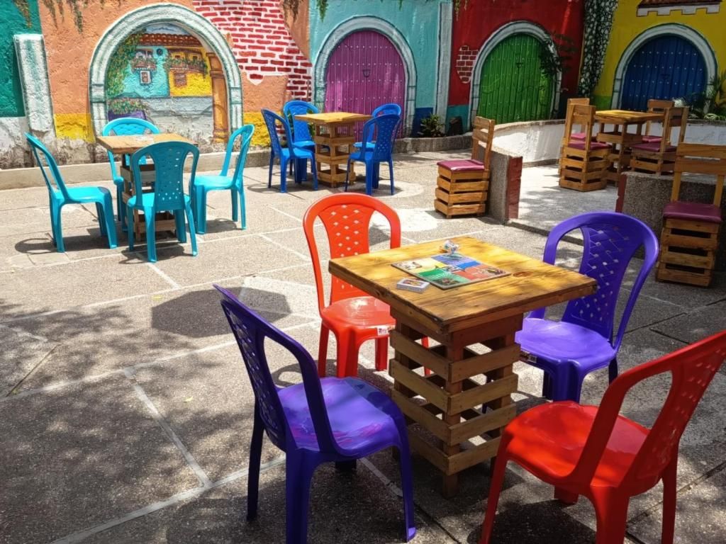 Área externa com mesas e cadeiras de plástico colorido, cercada por murais vibrantes e portas.