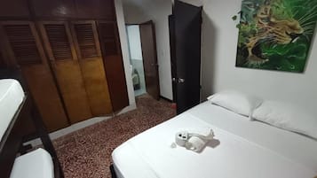 Quarto de hotel com cama, guarda-roupa, um quadro e banheiro visível através de uma porta aberta.