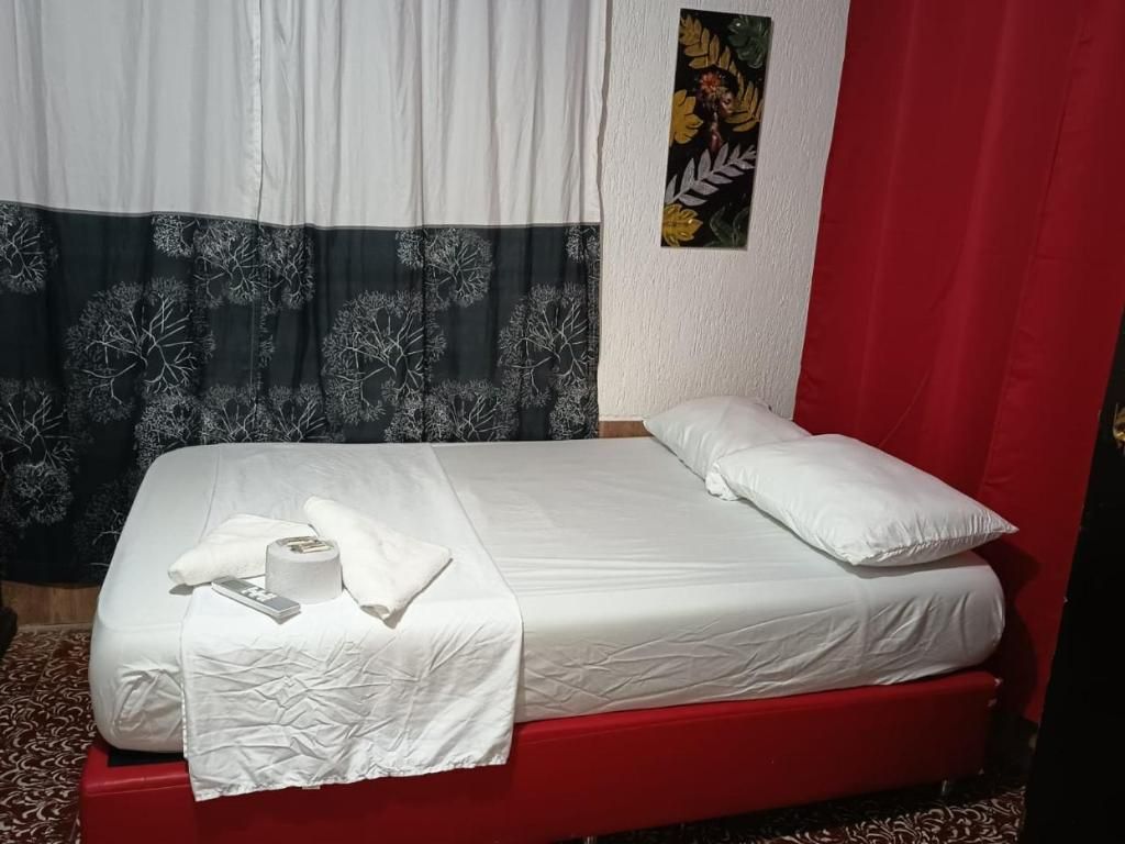 A single bed with white bedding, a red headboard, and a curtain with a tree pattern.