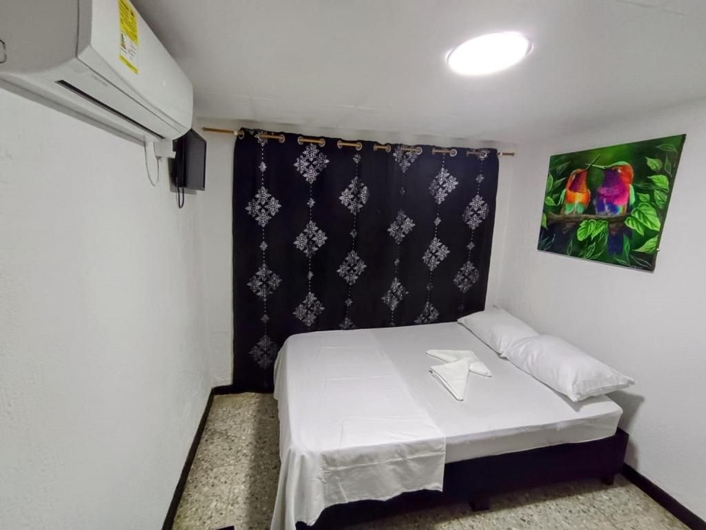 A small, neatly made room with a bed, a curtain, a wall-mounted air conditioner, and a picture of birds.