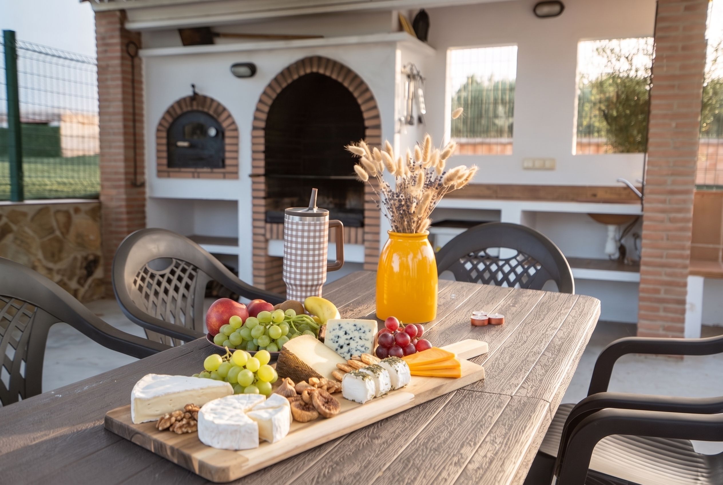 Un espace de restauration en plein air avec une table en bois dressée, sur laquelle on trouve du fromage, des fruits et des noix.