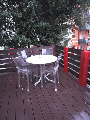 A round table with four clear plastic chairs on a wooden deck, surrounded by a wooden fence with red accents. - Vollmöbliertes 4-Zimmer-Haus in Pforzheim (Pforzheim)