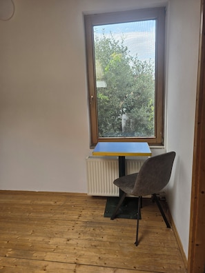 A room with a sloped ceiling, a radiator, a blue table, and a grey chair. - Vollmöbliertes 4-Zimmer-Haus in Pforzheim (Pforzheim)