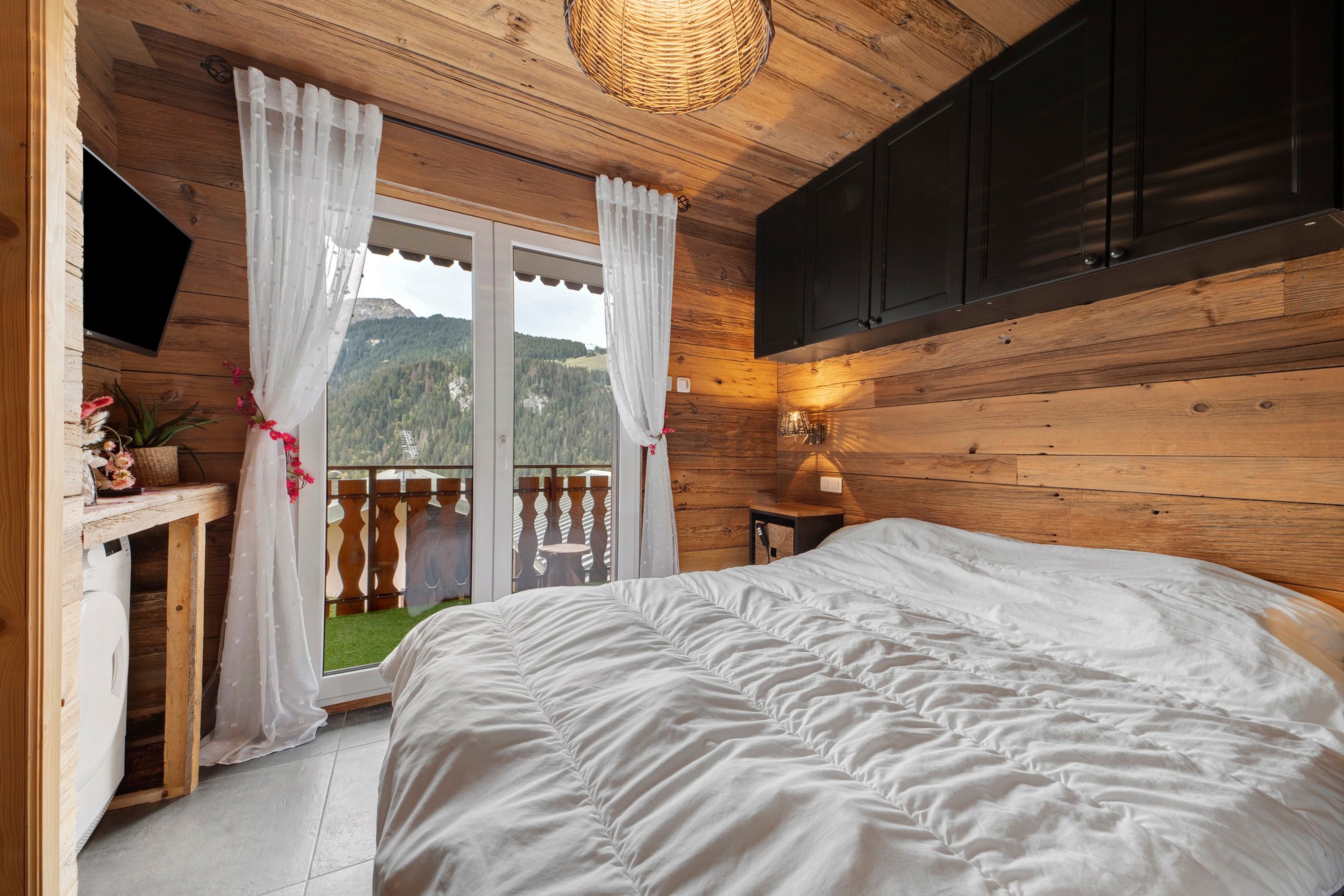 Une chambre à coucher comprenant un lit, un bureau, un téléviseur et donnant sur un paysage montagneux grâce à une porte coulissante.