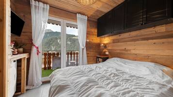 Une chambre à coucher comprenant un lit, un bureau, un téléviseur et donnant sur un paysage montagneux grâce à une porte coulissante.