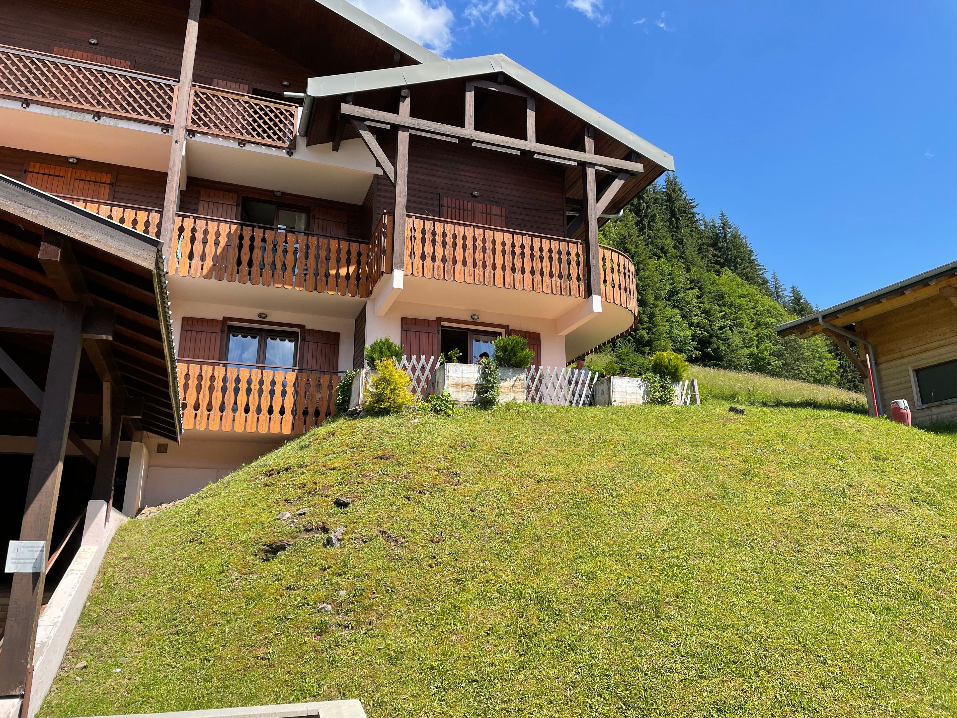 Un bâtiment en bois à plusieurs étages, doté de balcons et d’un toit en pente, avec une colline verdoyante au premier plan.