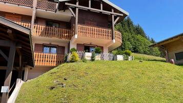 Un bâtiment en bois à plusieurs étages, doté de balcons et d’un toit en pente, avec une colline verdoyante au premier plan.