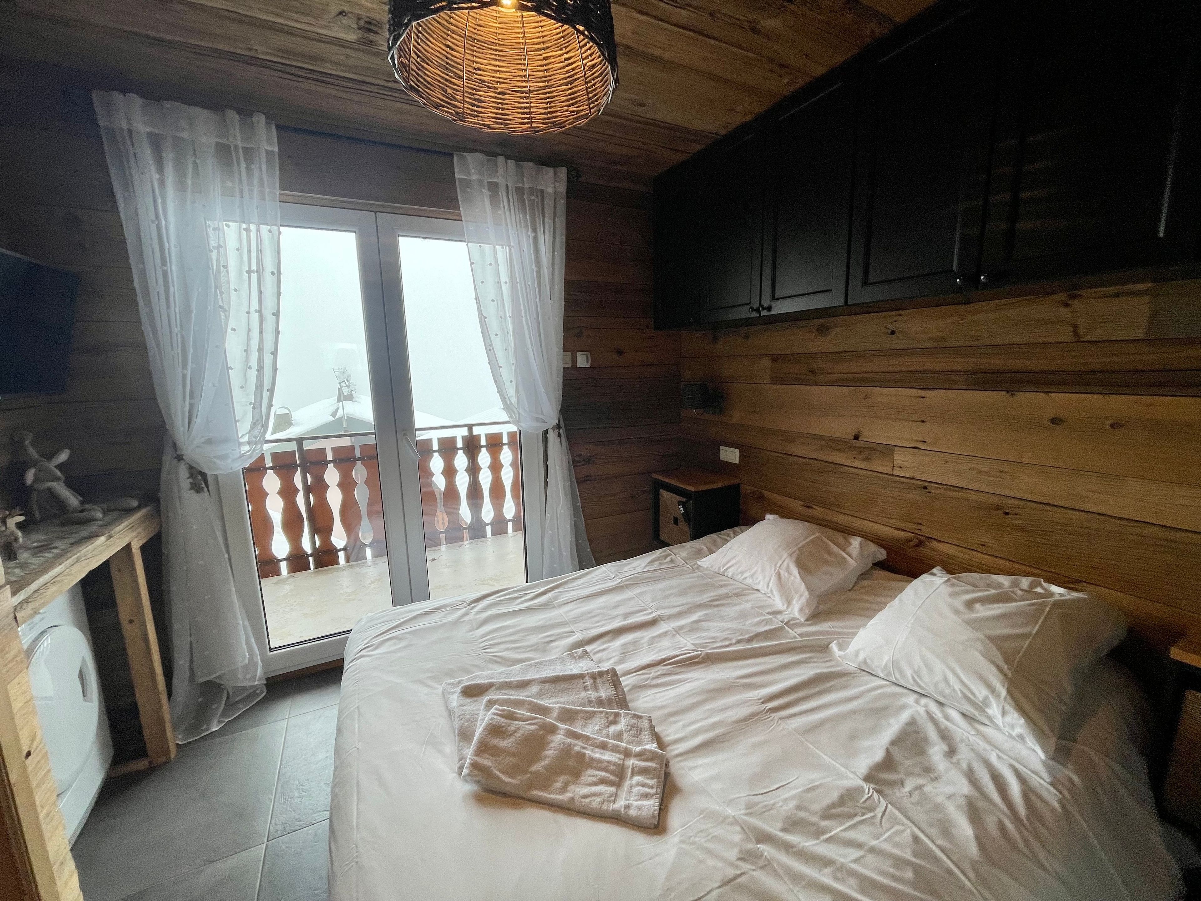 Une chambre avec un lit, une tête de lit en bois, une petite table de chevet et une fenêtre avec des rideaux.