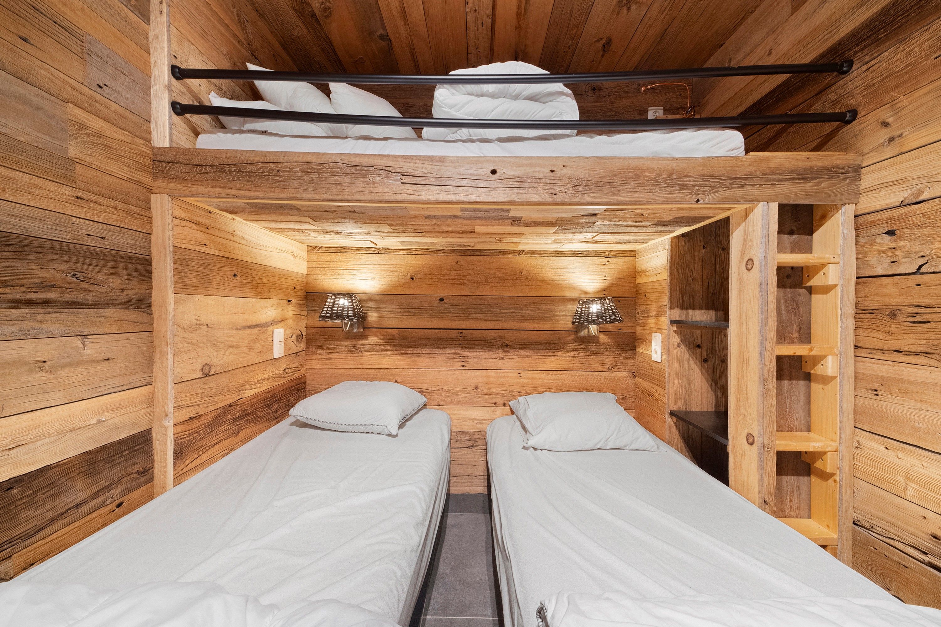 A compact wooden cabin with two single beds, a small shelf, and a slanted ceiling.