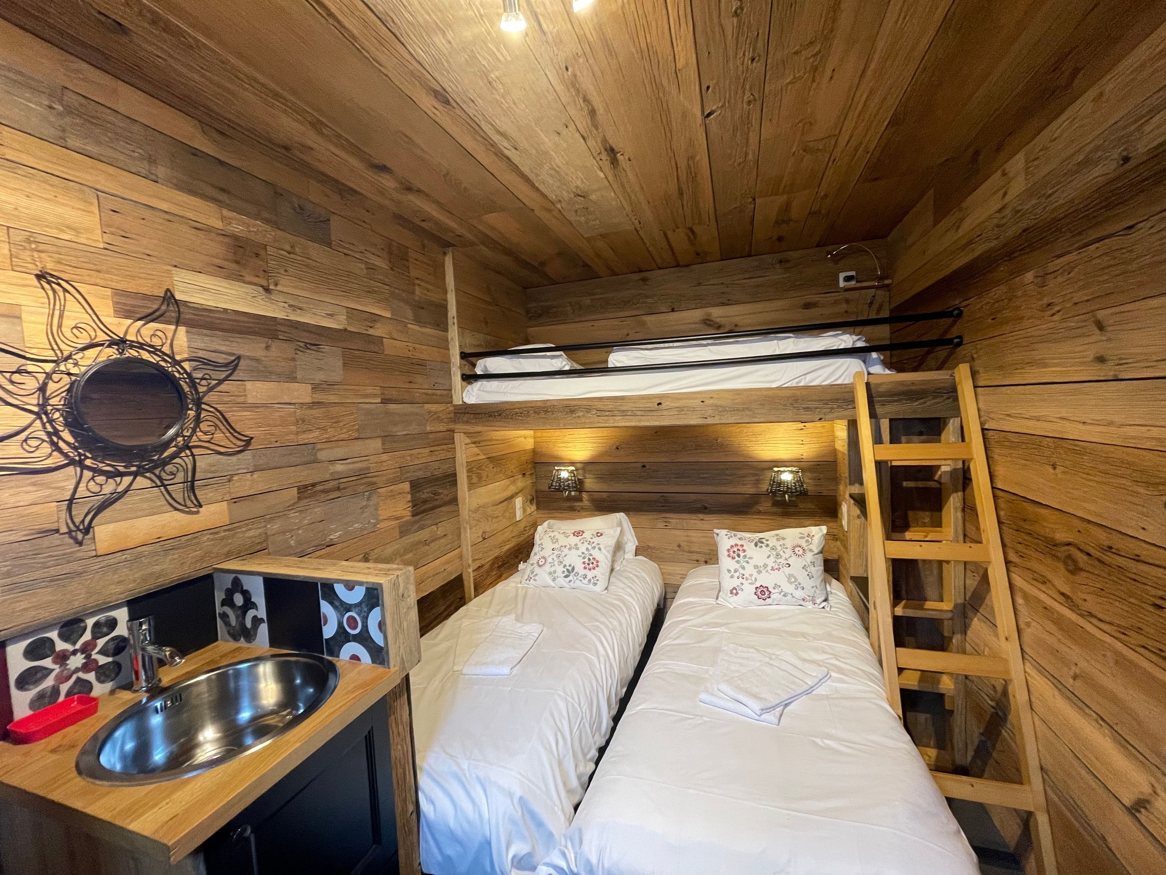 Une petite pièce avec un lit superposé, un petit lavabo et un miroir au mur.