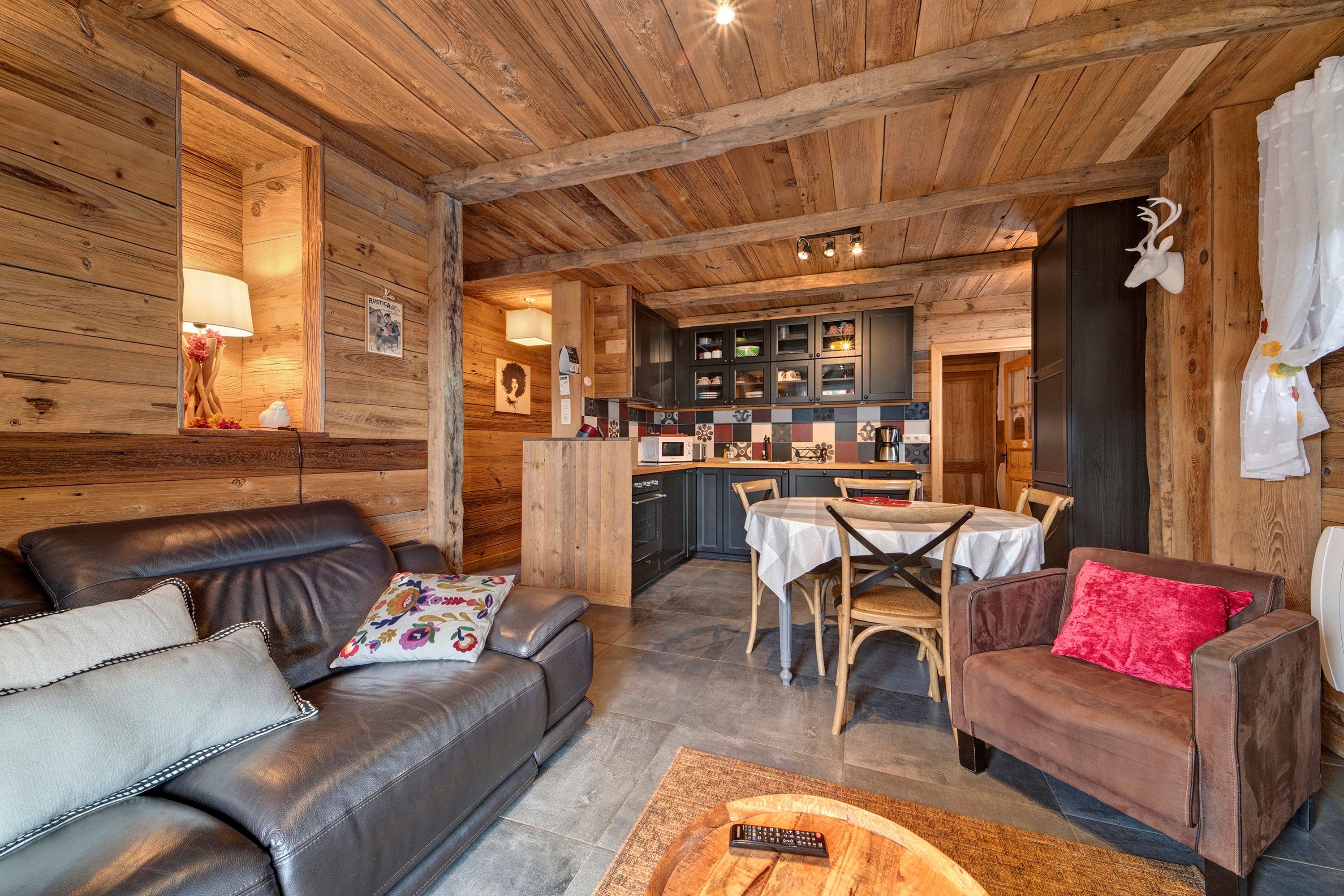 A cozy cabin interior with a leather sofa, a dining table with chairs, and a kitchen area with cabinets and a refrigerator.