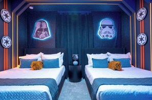 Ein Zimmer mit zwei Betten, jedes mit einem Kopfkissen und einem kleinen Hund. Es gibt zwei Wanddekorationen, eine zeigt Darth Vader und eine zeigt einen Sturmtrupplerhelm.