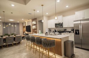 A modern kitchen with a central island, bar stools, and stainless steel appliances. - 7BR house sleeps 20 with game room and pool (Clermont)