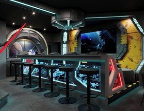 A futuristic bar area with high-tech bar stools, a large monitor displaying a space scene, and a red laser on the wall. - 15BR house with private pool in Sonoma Resort (Kissimmee)