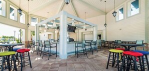 An outdoor patio area with multiple tables and chairs, a central bar area, and a TV screen. - 9BR house with game room near Disney (Kissimmee)