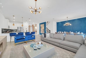 A modern living room with a sofa, chairs, a coffee table, and a dining area with a table set for a meal. - 9BR house sleeps 24 with hot tub and pool (Kissimmee)